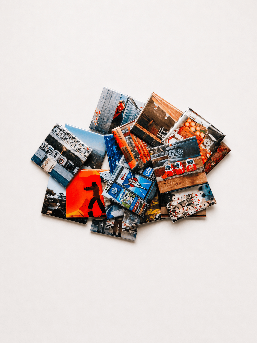 A loose pile of overlapping glossy photo magnets printed with colourful travel photos, on a pale tabletop
